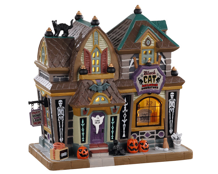 A gothic, but colorful building has a sign out front that reads Black Cat Halloween Decorations, as well as multiple black cats, pumpkins, skeletons and other signs. 