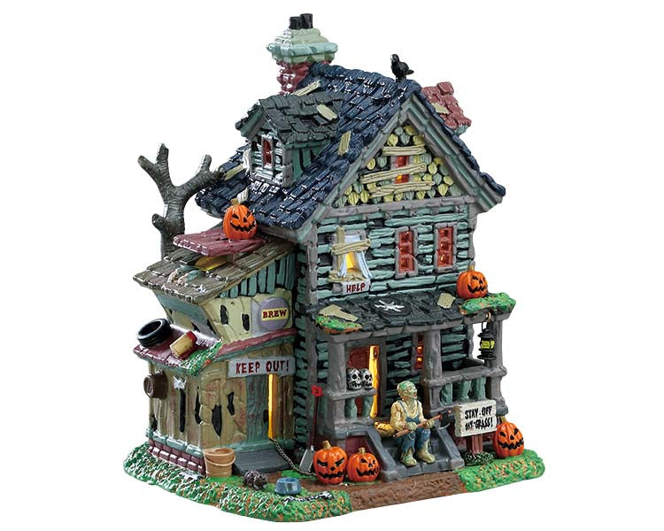 A dilapidated wooden house is covered in spooky jack-o'-lanterns and signs reading keep out. A sinister monster looking man sits on the front porch with an axe waiting for his next victim. 