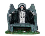 Lemax Spooky Town Reaper Bench #34608 at Eerie Emporium - A stone bench has a skeleton wearing a black robe with red eyes standing behind it.