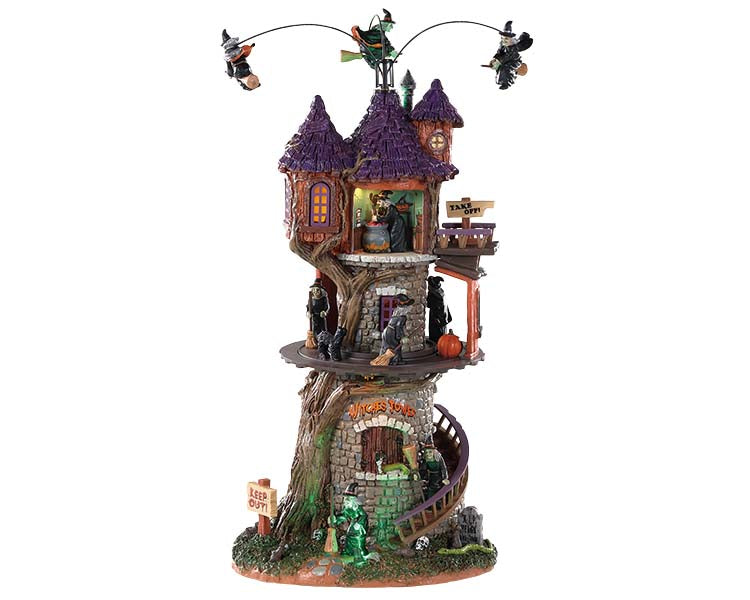 Lemax Spooky Town Witches Tower #85301 at Eerie Emporium - a massive stone building with a purple shingled roof has a winding wood staircase that runs up. There are three witches on brooms flying above it and numerous other witches below on, in and around the creepy structure.