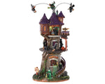 Lemax Spooky Town Witches Tower #85301 at Eerie Emporium - a massive stone building with a purple shingled roof has a winding wood staircase that runs up. There are three witches on brooms flying above it and numerous other witches below on, in and around the creepy structure.