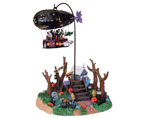 A blimp full of monsters revolves around a spooky and festive scene below that includes jack-o'-lanterns, tombstones and trees.