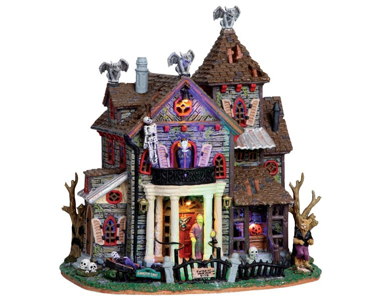 A Spooky residence with gargoyles on the peaks of the roof,  skeletons and monsters abound and exterior colored lighting that casts an eerie glow across the building.