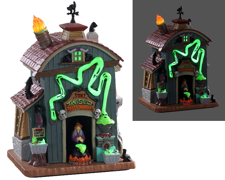 A small barn style building with a sign that reads "terribly twisted taffy-works" has various lighted green elements while a witch and her bubbling cauldron take center stage.