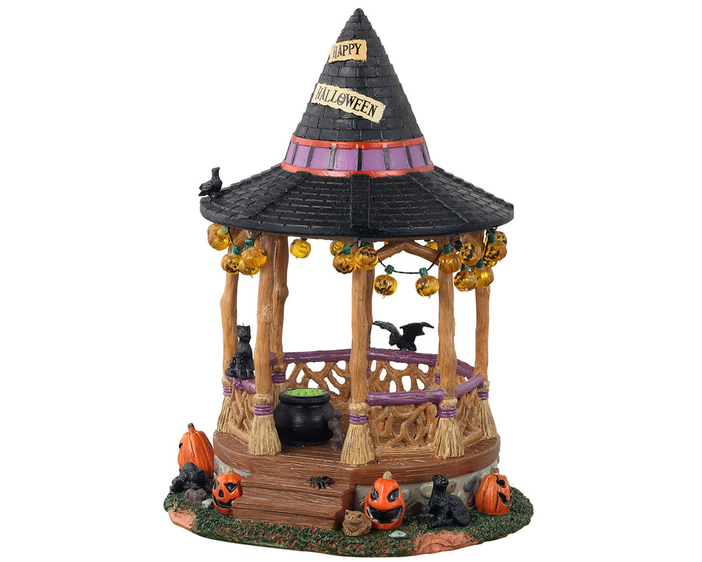 This Witch Gazebo is a charming Halloween table piece. The roof of the gazebo is shaped like a black witch's hat. Hanging from the roofline, you can see a string of pumpkin lights. The gazebo's columns are built from witches' brooms. Inside, you can see a cauldron bubbling, with a trusty black cat and a black bat keeping watch.