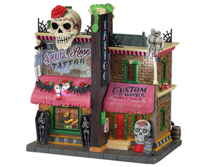 
            
                Load image into Gallery viewer, A brick tattoo shop called Skull Rose Tattoo has a large skull on top of it, as well as snakes, skeletons and coffins. 
            
        