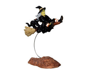 
            
                Load image into Gallery viewer, A witch dressed in black sits atop a wire that makes it appear as though she&amp;#39;s flying. Her black cat sidekick rides on her broom behind her.
            
        