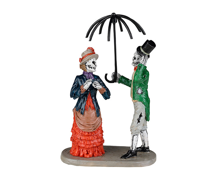 A Victorian dressed skeleton couple stands next to each other. The man holds a dilapidated umbrella over the head of the woman. 