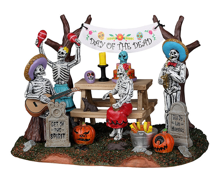 Festive skeletons celebrate The day of dead with drinks, sombreros, music and spooky cake. There's tombstones and jack o' lanterns on the ground in front of them. 