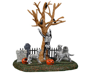 A skeleton tries to run up a withered tree away from skeleton dogs that are chasing him. There are tombstones, jack o' lanterns and crows all around.