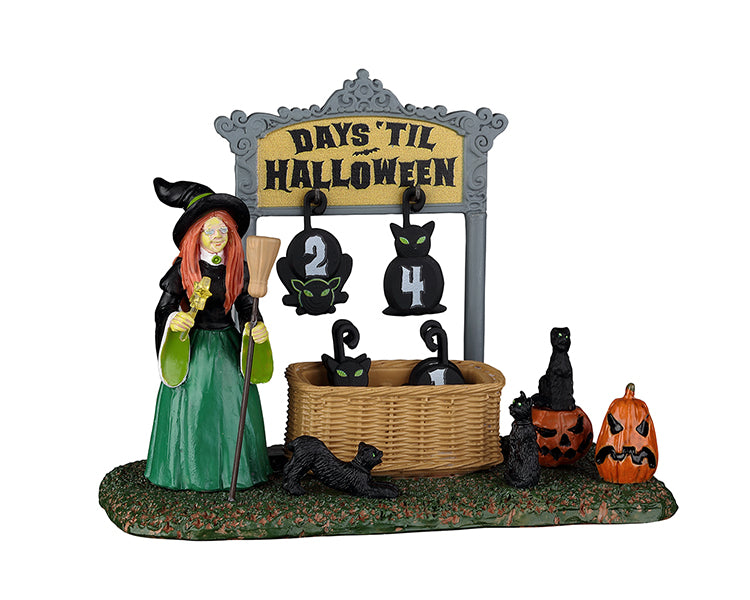 A witch stands next to a sign that reads, "Days Til Halloween" while surrounded by black cats. The countdown pieces that are added to the sign are shaped as black cats.