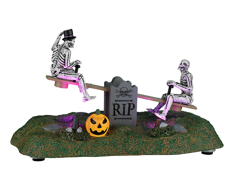 A see-saw over a tombstone is occupied by two skeletons. a jack o' lantern sits in front.