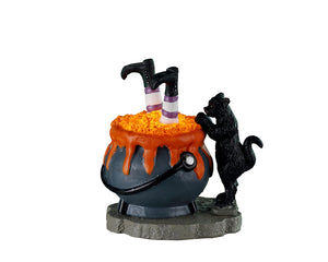 A bubbling boiling cauldron has a pair of witch legs and feet sticking out of it. The witch's black cat sidekick looks on in horror.