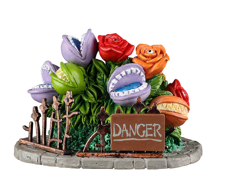 A large bush is full of colorful carnivorous plants. In front of the plants is a sign that reads danger.