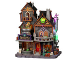 A large grey and purple building called Agatha's Apothecary in covered in witches and skeletons.  There's a bright red door as well as frogs and jack o' lanterns around.