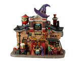 Lemax Spooky Town Toil & Trouble Alehouse #25852 - A whimsical stone building has a large purple witch hat on top of it and multiple bubbling cauldrons of beer. In the center of the building are three sinister witches brewing ale while a skeleton orders a beer from a ghoulish bartender on the right side of the structure.