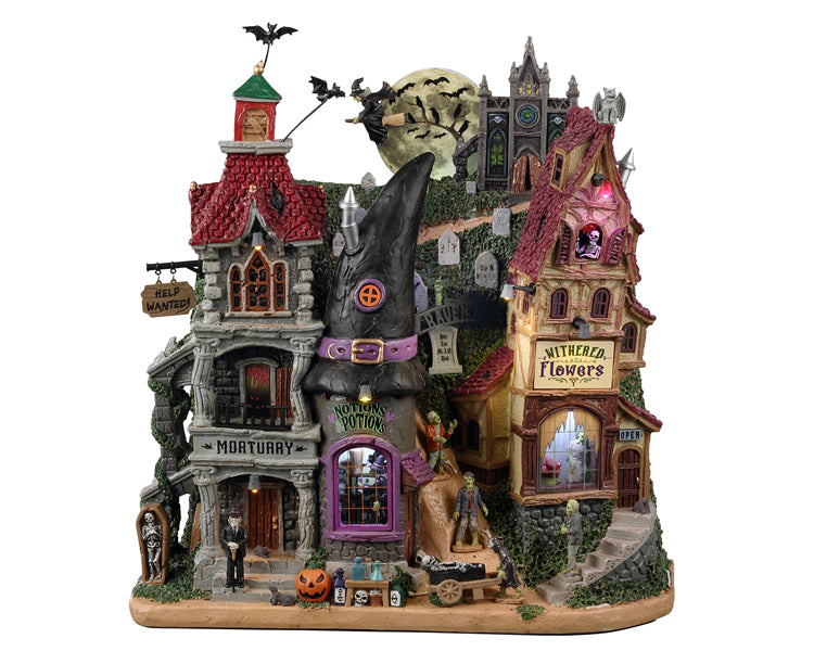 Lemax Spooky Town Raven Hill #25919 - A multi layered scene depicts a Halloween Village similar to something out of a Tim Burton film with numerous spooky buildings including a mortuary, notions potions and a withered flowers shop. Numerous monsters and tombstones, plus an ominous moon with a witch and bats in front of it make this piece extra creepy.