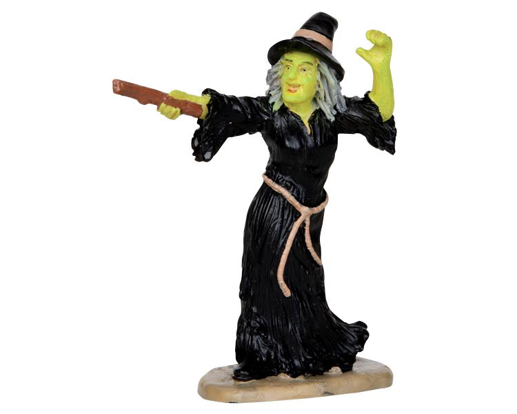 A green witch dressed in black raises her wand to cast a spell. 