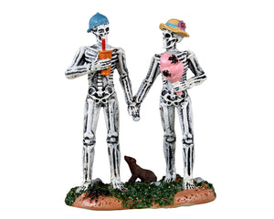 Lemax Spooky Town Spooky Carnival Date #32194 - A skeleton couple holds hands while the man drinks out of an orange soda cup and the woman eats pink cotton candy covered in spiders.