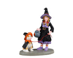 Lemax Spooky Town No Chocolate For You! #32198 - A girl wearing a light purple and black witch costume holds a cauldron trick or treat bucket in one hand and a leash attached to her puppy that is also wearing a costume.