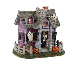 Lemax Spooky Town Ghost Cottage #34080 - A purple house with a grey roof has numerous ghosts peaking through windows while jack o' lanterns and a grey fence are out front.