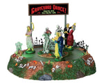 Multiple zombies dance around two skeletons that are playing music while a sign reads "Graveyard Dance!" behind them. 