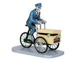 A spooky skeleton dressed as a postman peddles a green bike with a box on the front that reads, "Midnight Mail Delivery". Inside the box peaks out a monster with green hands.