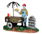 A skeleton hot dog vendor with a red hat sells horror hot dogs out of their coffin cart. 