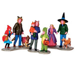 A large group of trick-or-treaters including 3 adults, 2 dogs and 4 children in various different costumes walk together in search of more candy.