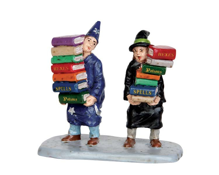 A young wizard and witch stand next to each other carrying books stacked to their heads.