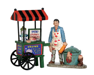 A sinister zombie sells human parts out of his wheeled food cart. Parts include brains, eyeballs and limbs. On the ground next to him is a container full of addition body parts and a boot with a bloody leg protruding. 