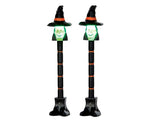Black and orange lamp posts are illuminated above by lighted cute green witch faces.