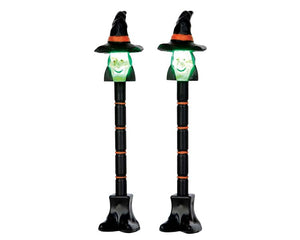 
            
                Load image into Gallery viewer, Black and orange lamp posts are illuminated above by lighted cute green witch faces.
            
        