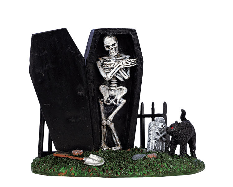 A creepy cemetery scene is shown where a black coffin is open and inside is a skeleton. A spooky black cat and tombstone are to the right of the coffin, while a small iron fence is positioned behind the coffin.