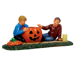 
            
                Load image into Gallery viewer, A dad lays next to his son and teaches him how to properly carve his first jack-o&amp;#39;-lantern while the son eagerly scrapes away any remain pumpkin insides. 
            
        