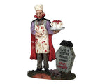 An evil vampire covered in blood, wearing a cape and chefs hat holds a tray with two mugs full of blood while he stands next to a tombstone.