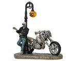 A creepy, but cool skeleton wearing a leather jacket and blue jeans leans against a pumpkin light pole and his motorcycle made of bones. 