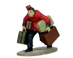 A hunched over monster bellboy dressed in a red long sleeve shirt and hat struggles to carry 4 pieces of luggage.