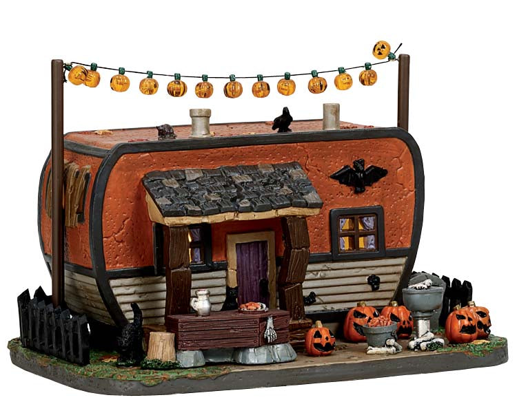 An orange and grey camper sits underneath mini pumpkin string lights and behind creepy jack-o'-lanterns and black cats.