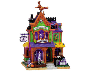A bright green, purple and brown colored Halloween costume shop building. The building has exterior lighting that surrounds and illuminates it while monsters & masks in the window make this building especially spooky and fun! 