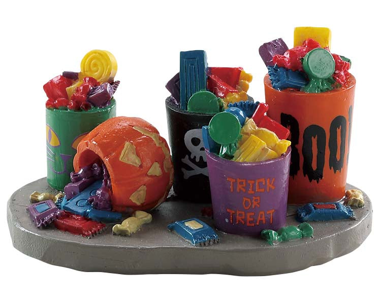 4 Buckets of candy are overflowing with candy while a pumpkin has toppled over spilling out candy around it. 