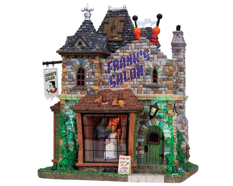 A brick building is illuminated by green lights that shine on the front walls left and right alternately. A sign hangs on the front left with a picture of Frankenstein under the writing Frank's Salon while Frank's Salon also appears in big purple letters on the main front brick portion of the building. In the main window Frankenstein cuts his brides hair. 