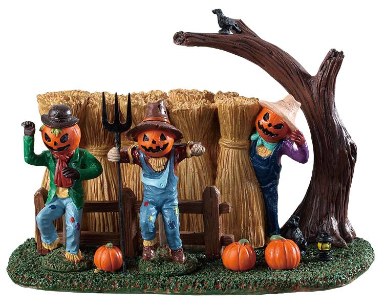3 sinister pumpkin faced scarecrows stand guard over a row of crops. 