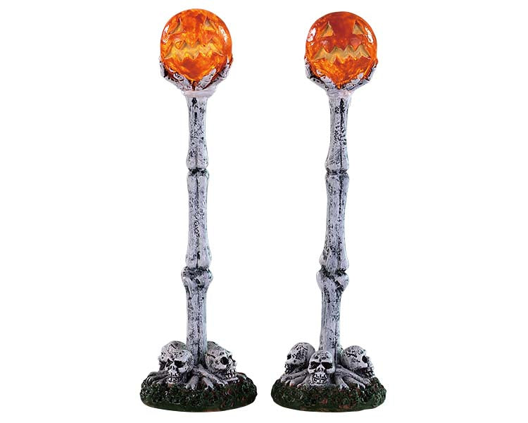 Two lamp posts made of bone are illuminated at the top by spooky jack o' lanterns. Skulls are on the ground at the base of the light posts.