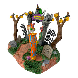 Retired Lemax Spookytown Carnival Gate #33013 - A sinister clown stands in front of a gothic gate that has a purple sign that reads "Spookytown Carnival"