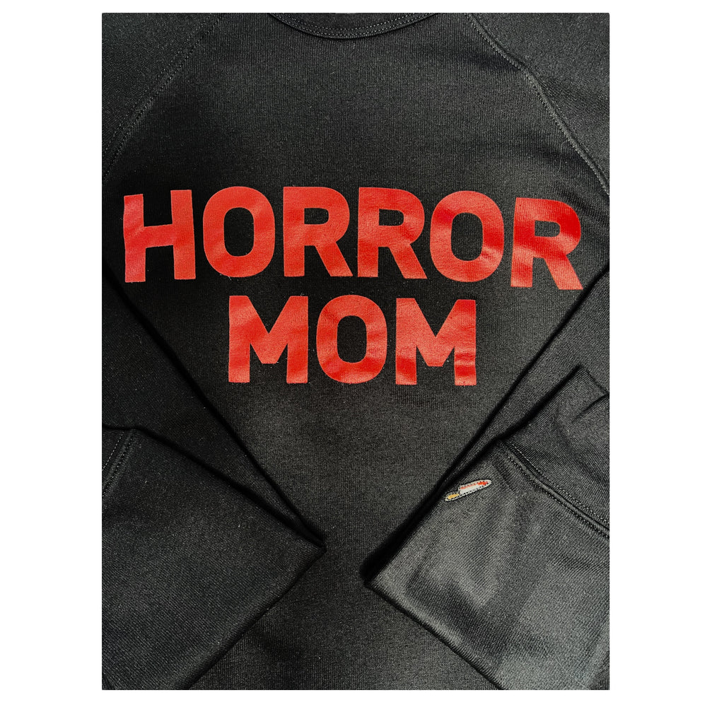 A black crewneck that has HORROR MOM across the chest in red and an embroidered knife on the sleeve