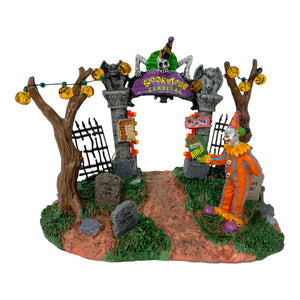 Retired Lemax Spookytown Carnival Gate #33013 - A sinister clown stands in front of a gothic gate that has a purple sign that reads "Spookytown Carnival"
